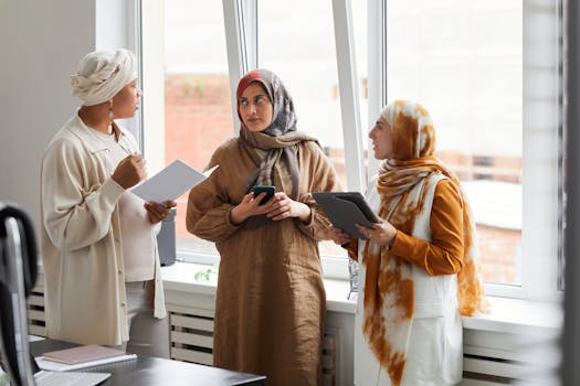 Three women in smart casual attire discuss work in a modern office setting.